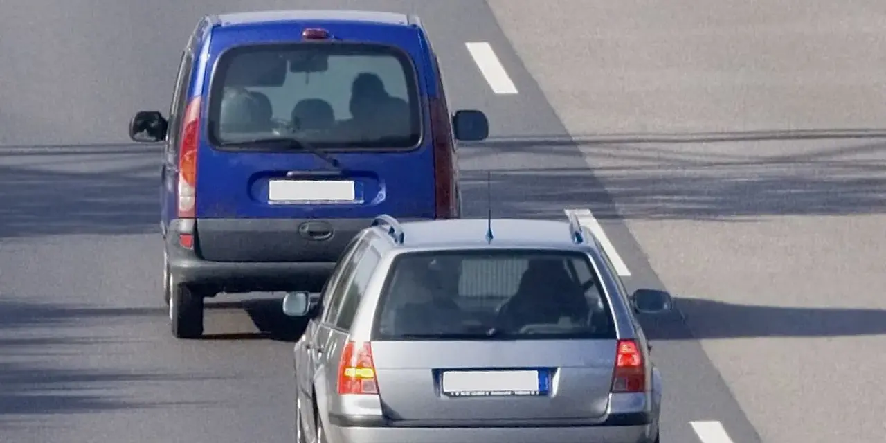 Un veicolo che precede, una monovolume blu, è seguito da un'auto station wagon argentata su una strada asfaltata con segnaletica bianca.
