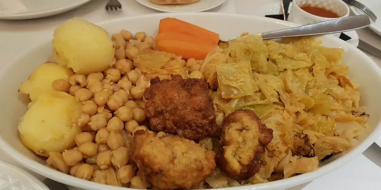 Un plato generoso de cocido madrileño con garbanzos, patatas, zanahoria, repollo y trozos de carne frita.