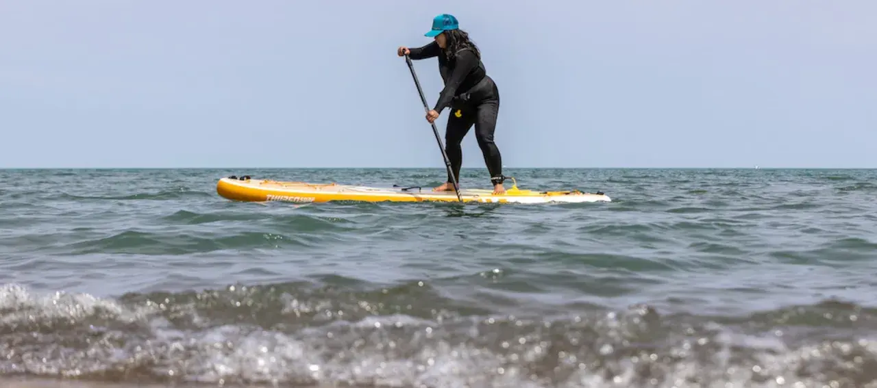 Frau auf einem gelben Stand Up Paddle Board im Meer, mit Paddel in der Hand.