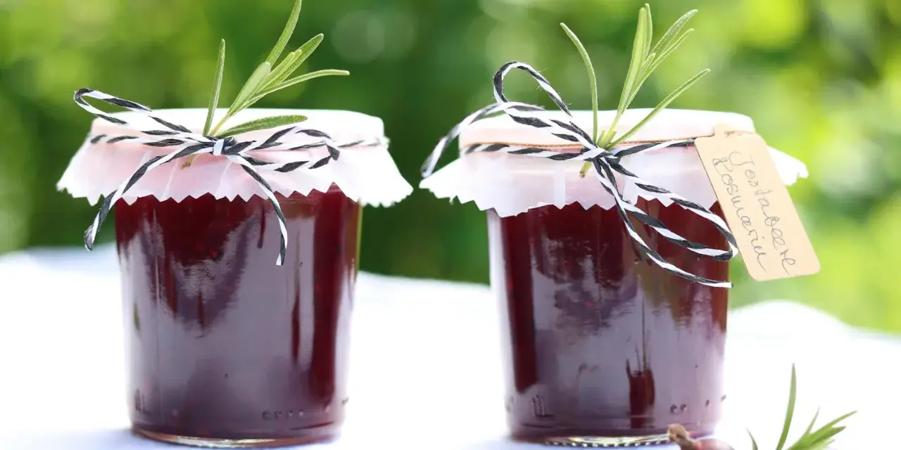 Zwei Gläser Jostabeere-Marmelade, liebevoll mit Rosmarin und kariertem Band verziert. Perfekt für die Jostabeere Verwendung auf Brot.