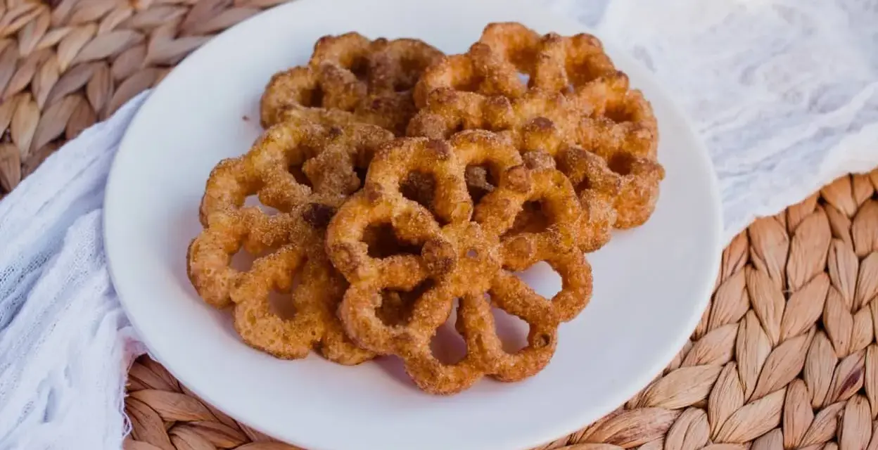 Buñuelos dorados con azúcar y canela en un plato blanco.