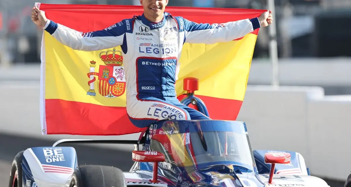 Alex Palou celebra su victoria en las 500 millas de Indianápolis, ondeando la bandera de España sobre su coche de carreras.