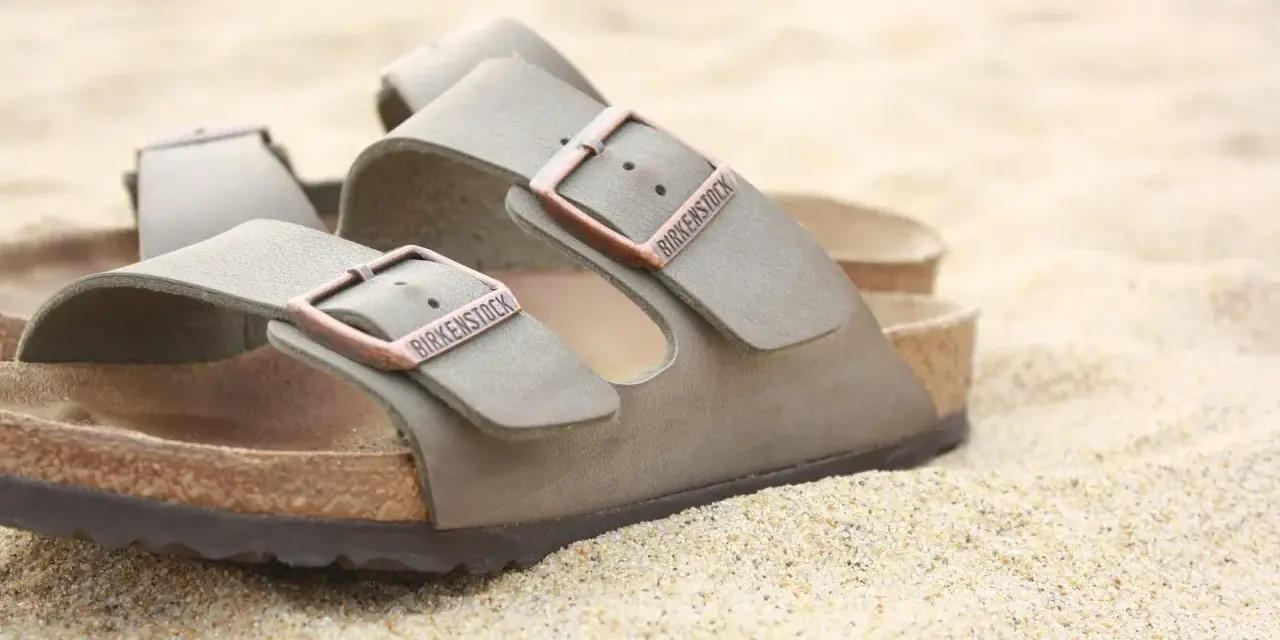 Sandali Birkenstock grigi sulla sabbia. Scopri come si lavano le Birkenstock per mantenerle perfette.