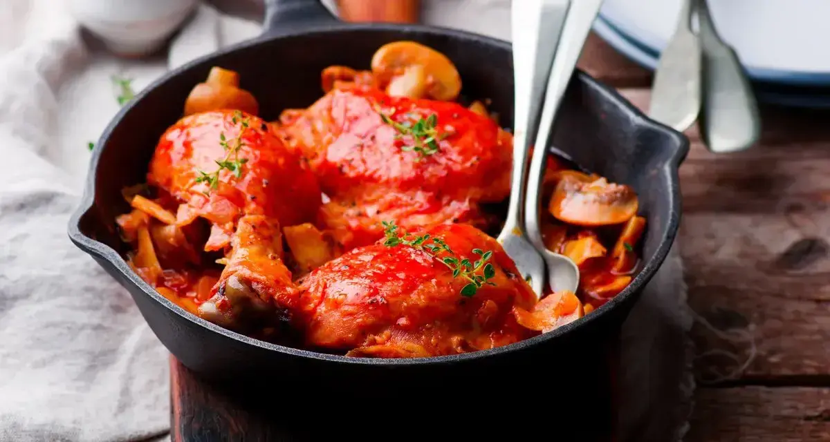 Pollo alla Marengo succulento in padella con funghi e pomodoro, guarnito con timo fresco.