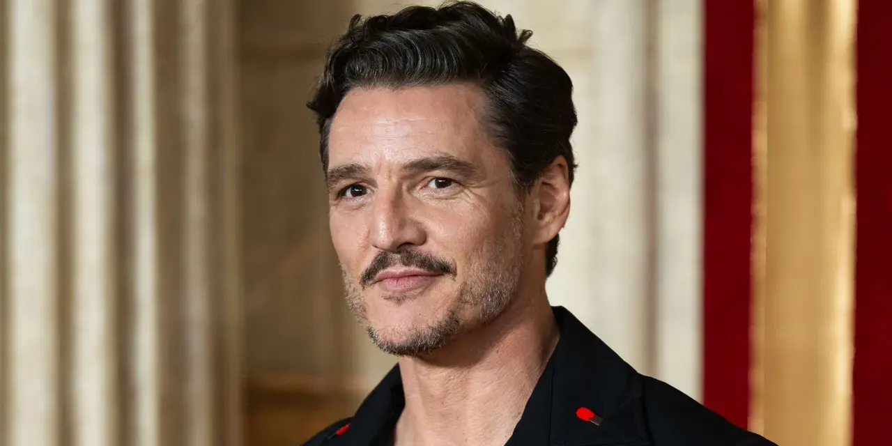 Pedro Pascal con cortes de pelo hombre corto por los lados y largo arriba, luciendo un pin de cerilla en su solapa.