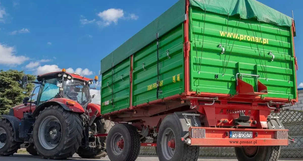 Czerwony traktor z zieloną przyczepą. Dowiedz się, jakich przyczep nie trzeba rejestrować, by ułatwić sobie pracę w gospodarstwie.
