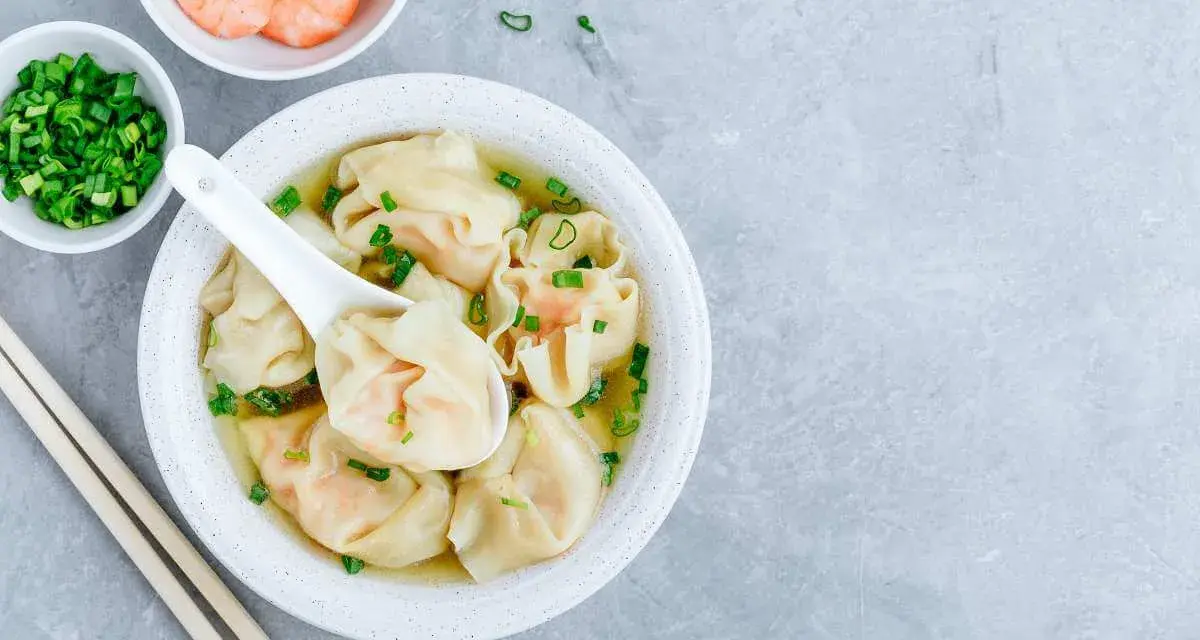 Aksamitna zupa wonton z krewetkami i szczypiorkiem, podana z pałeczkami.