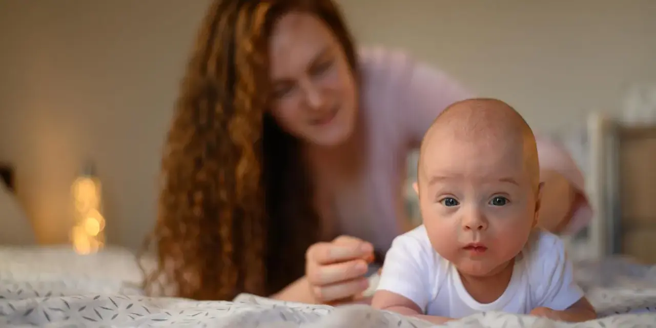 Maluch ćwiczy mięśnie szyi, kiedy układać noworodka na brzuchu. Mama czuwa z tyłu.