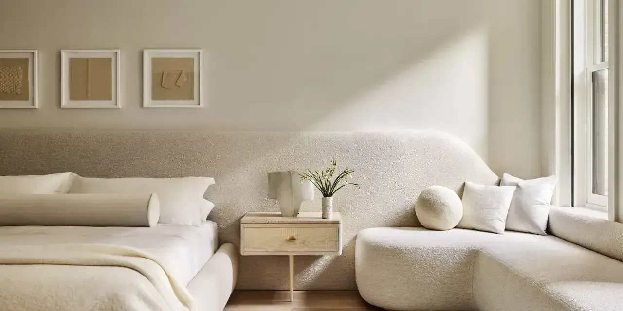 Dormitorio con decoración minimalista, cama baja, sofá curvo y arte abstracto en tonos tierra.