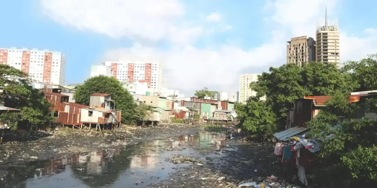 Un río lleno de basura y aguas residuales, rodeado de casas precarias y edificios modernos, ilustra los graves tipos de contaminación que afectan a esta comunidad.