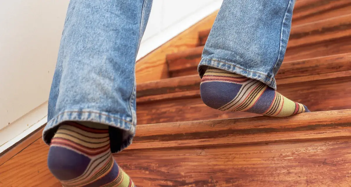 Füße in bunten Socken steigen eine Holztreppe hinauf, die auf eine Renovierung wartet.
