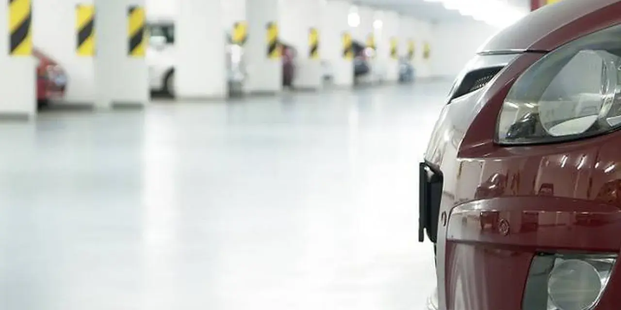 Czerwony samochód na tle rzędu miejsc parkingowych. Zastanawiasz się, ile miejsc parkingowych na mieszkanie jest dostępne?