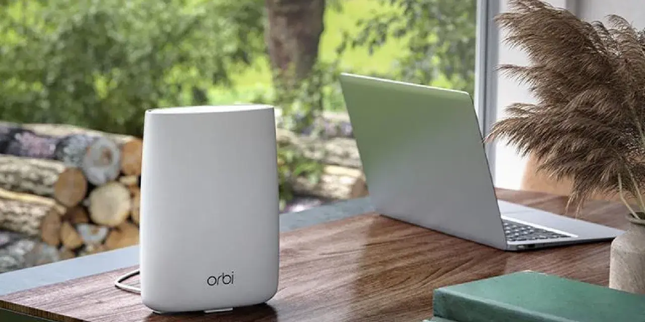 Ein weißer Orbi WLAN-Router steht neben einem Laptop auf einem Holztisch.