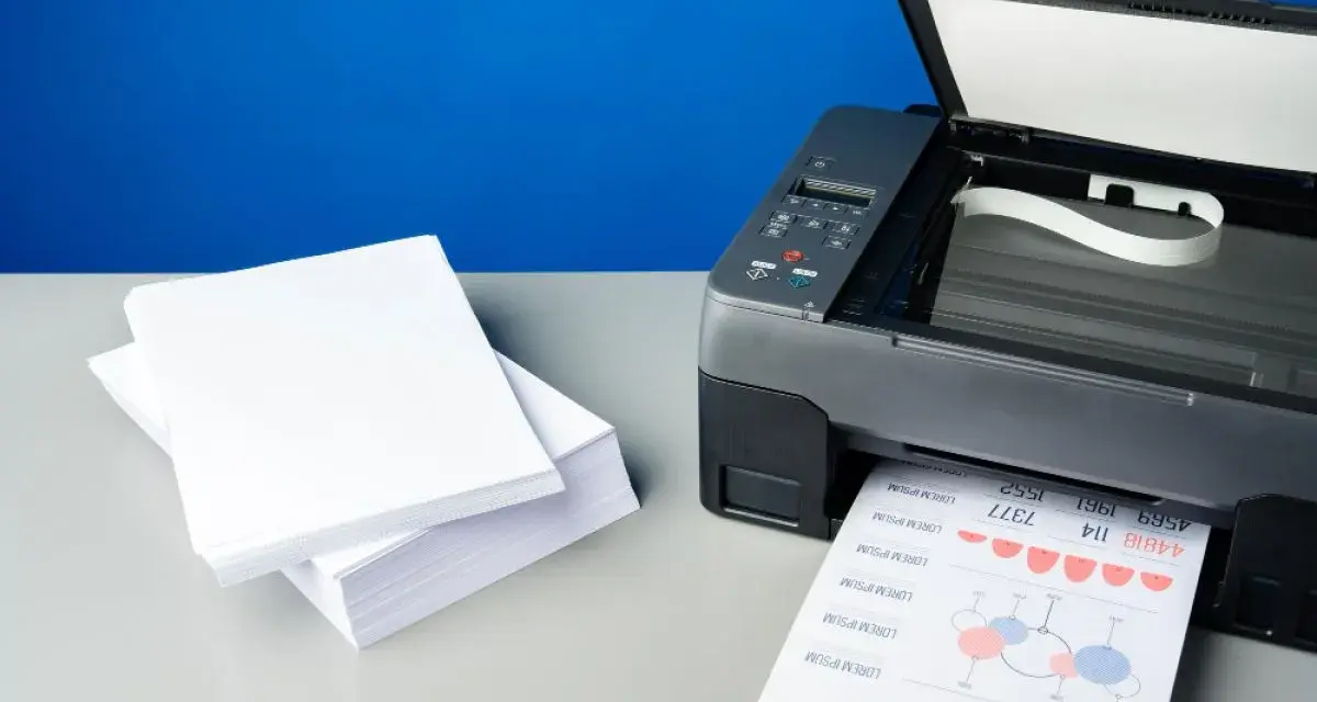 Stos białego papieru obok drukarki, która właśnie drukuje dokument. Różne rodzaje papieru do druku.
