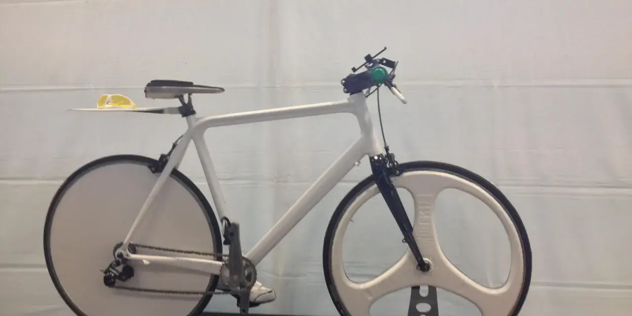A sleek, white 3d printed bike with unique disc and tri-spoke wheels. Yellow sunglasses rest on the seat.