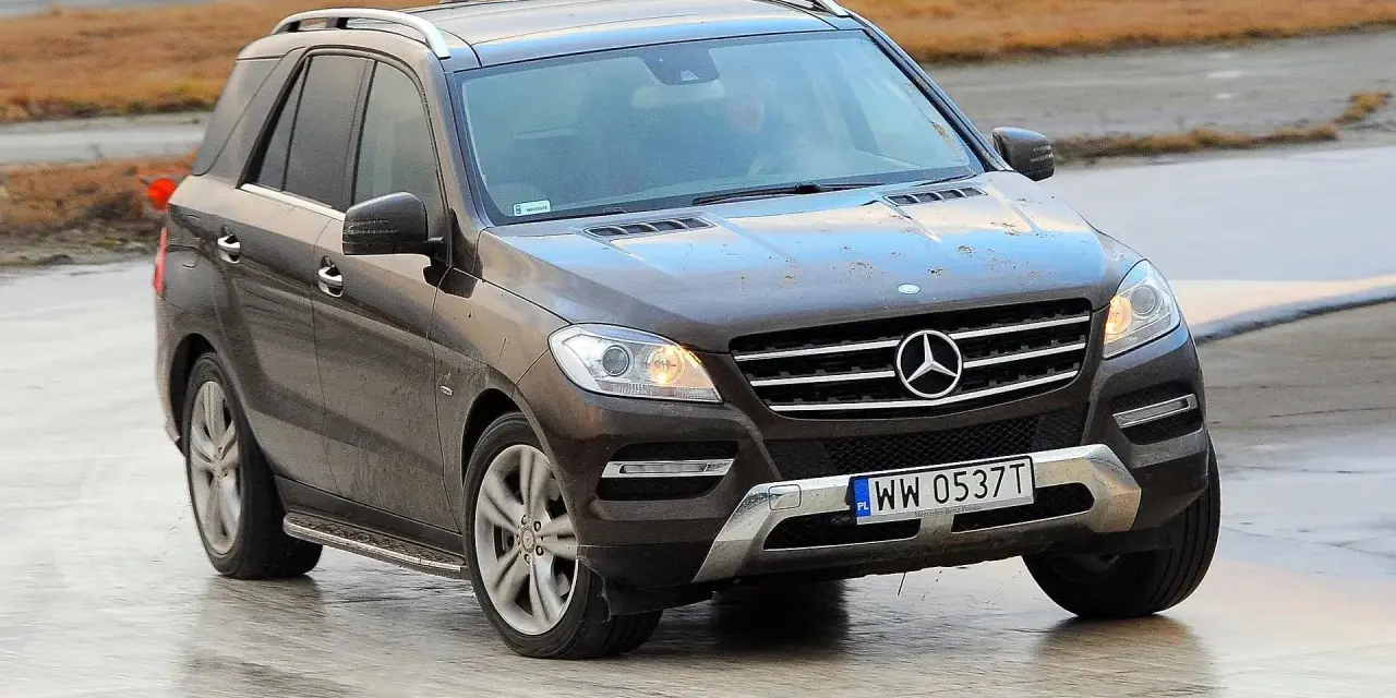 Brązowy Mercedes-Benz ML na mokrej nawierzchni, z widoczną tablicą rejestracyjną WW 0537T.