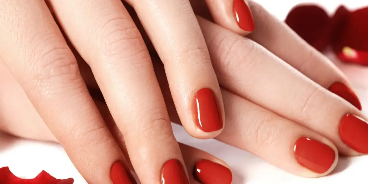 Dłonie z idealnym, czerwonym manicure tytanowym, otoczone płatkami róż.