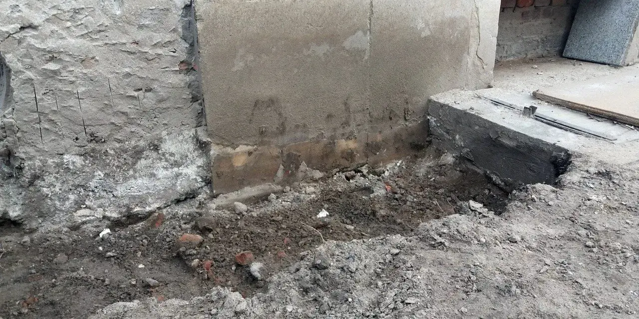 Odsłonięty fundament z cegły, ziemia i gruz wokół. Trwa remont.