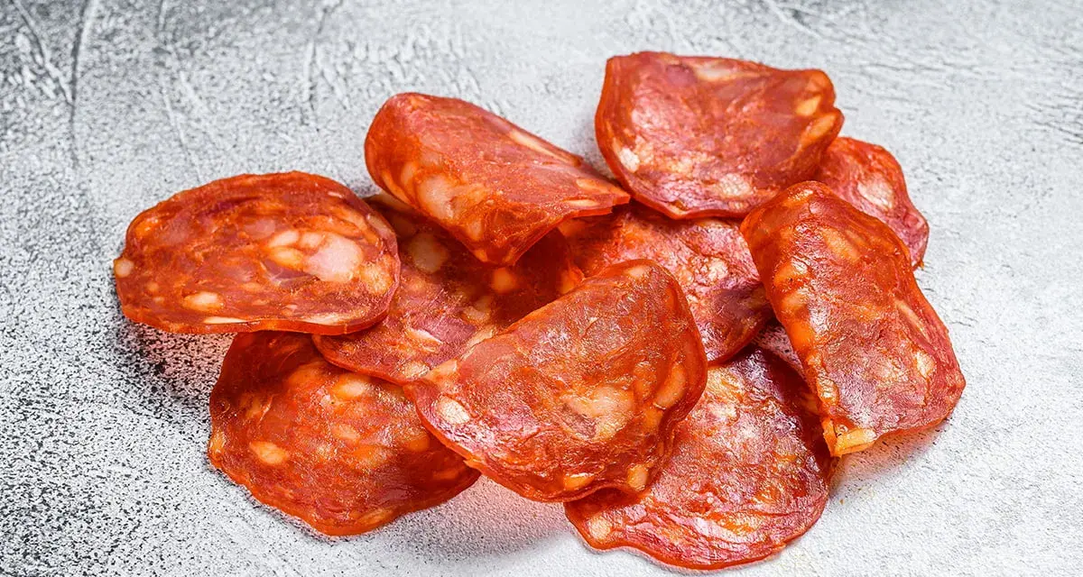 Plasterki pikantnego chorizo, wędzonej kiełbasy wieprzowej, z widocznymi kawałkami tłuszczu.