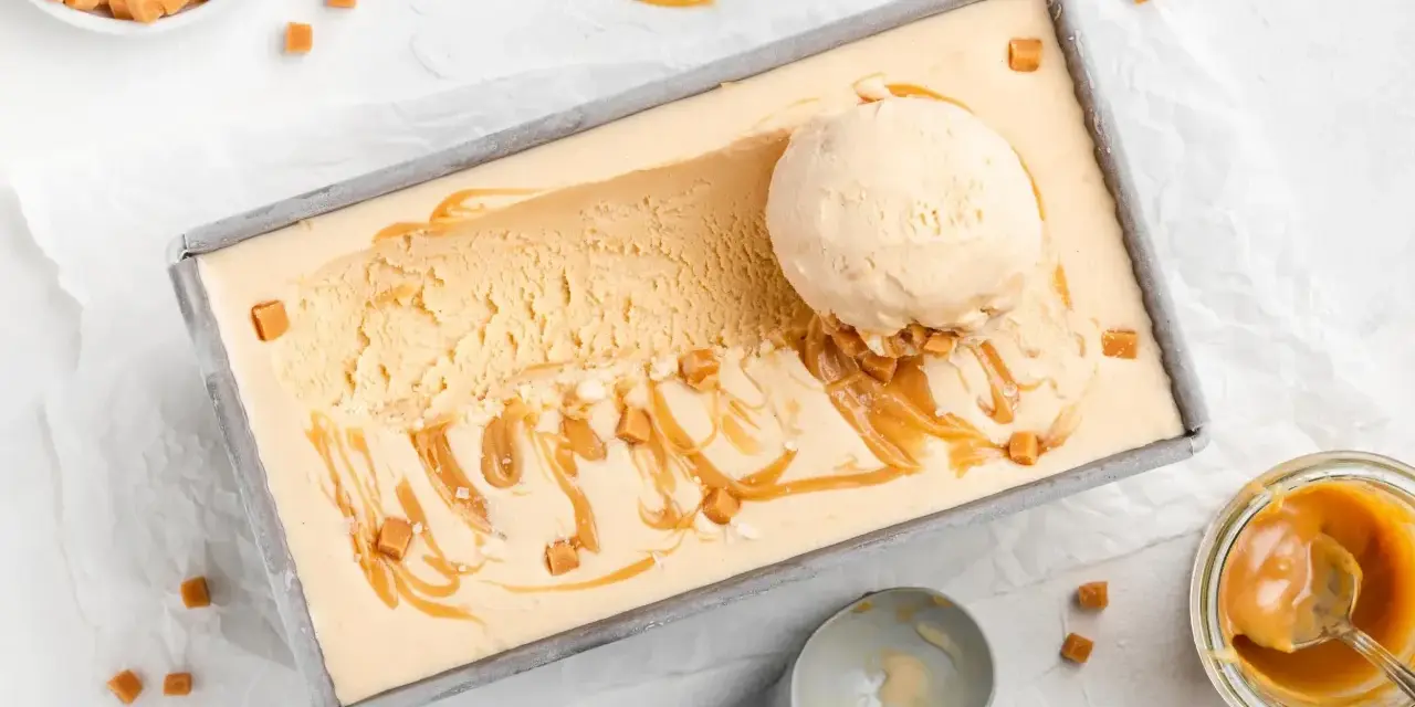 Ein Blech mit cremigem, hellbraunem Salted Caramel Eis, garniert mit Karamellsauce und kleinen Karamellwürfeln. Eine Eiskugel liegt darauf.