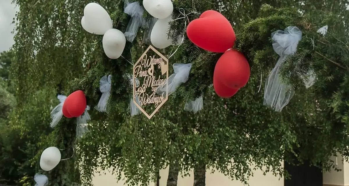 Brama weselna z balonami i napisem "Witamy Parę Młodą". Tradycja bram weselnych to symboliczne powitanie nowożeńców przez gości.