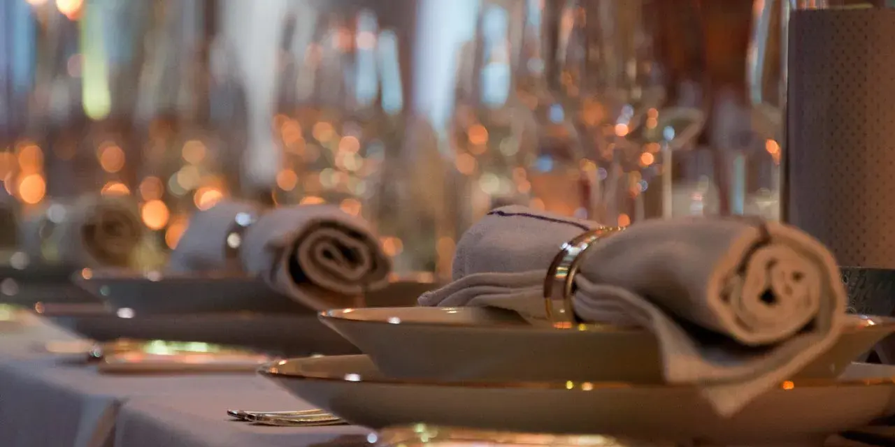 Ett elegant dukat bord med rullade servetter, hållna av en gyllene organza band-liknande ring. Mjuk belysning skapar en varm atmosfär.