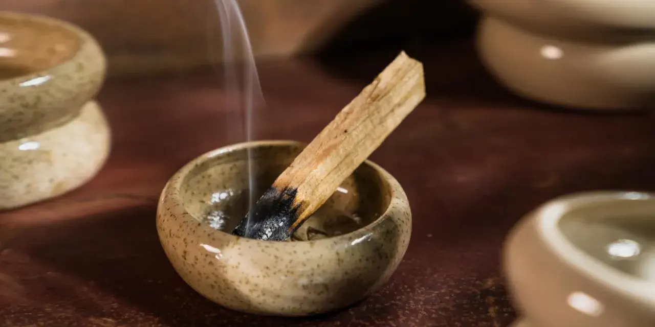 Dymiący patyczek palo santo w ceramicznej miseczce, unoszący się zapach wypełnia przestrzeń.