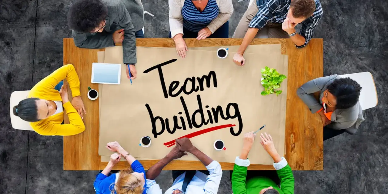 Un groupe diversifié autour d'une table discute de "team building". Ils collaborent, partageant des idées pour renforcer leur unité.