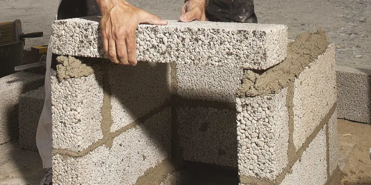 Byggare lägger mura lecablock på betongplatta. Murbruket syns mellan blocken.
