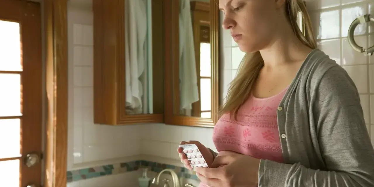 Zmartwiona ciężarna kobieta trzyma blister tabletek. Czy amoksycylina w ciąży jest bezpieczna?