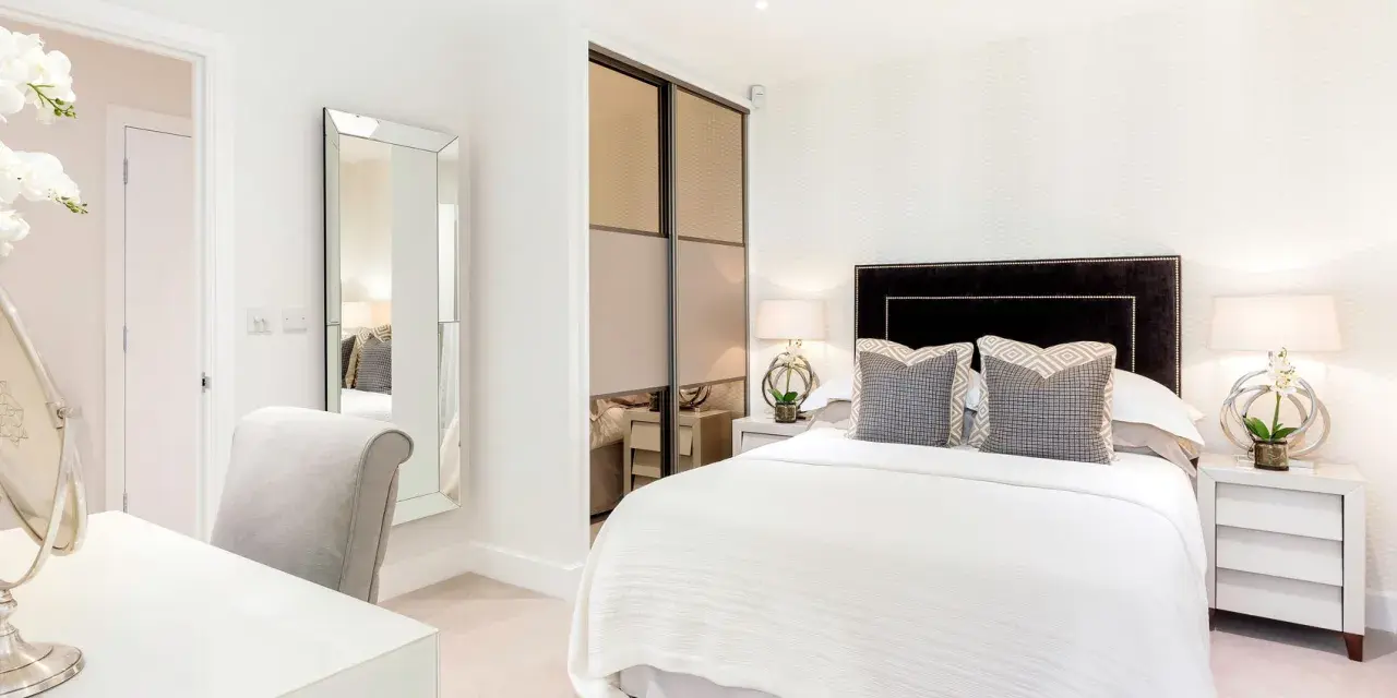 Elegante camera da letto senza finestra, con letto bianco, specchio a figura intera e un angolo toeletta.