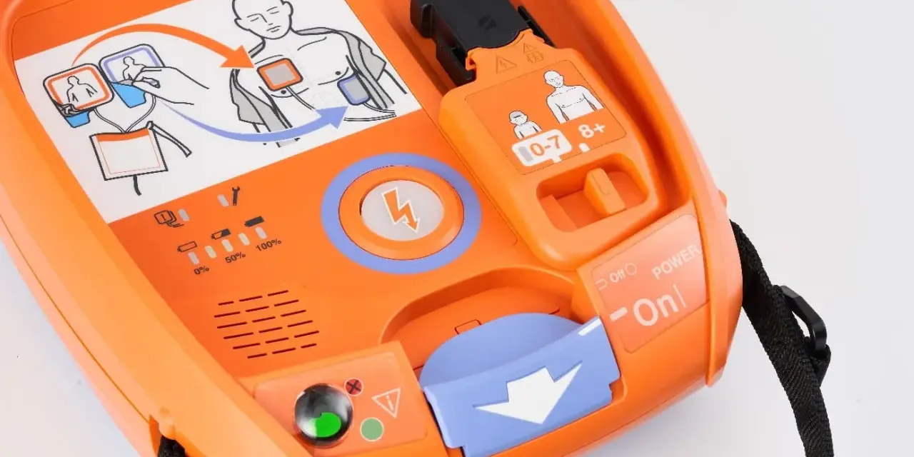 Pomarańczowy defibrylator AED z instrukcją użycia i wskaźnikami.