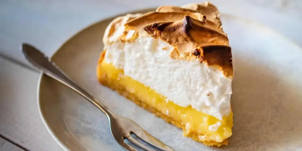 Rebanada de lemon pie con merengue dorado y relleno cremoso, lista para ser disfrutada con un tenedor.