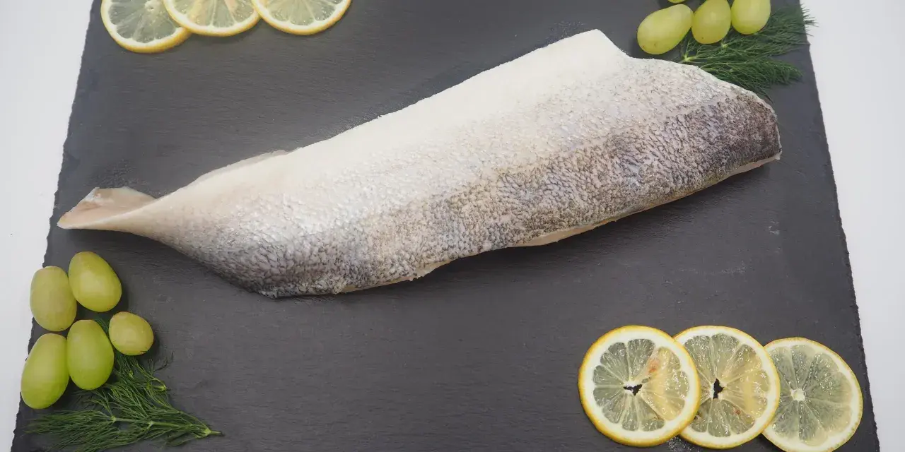 Filet ryby na czarnej desce z plasterkami cytryny, winogronami i koperkiem.