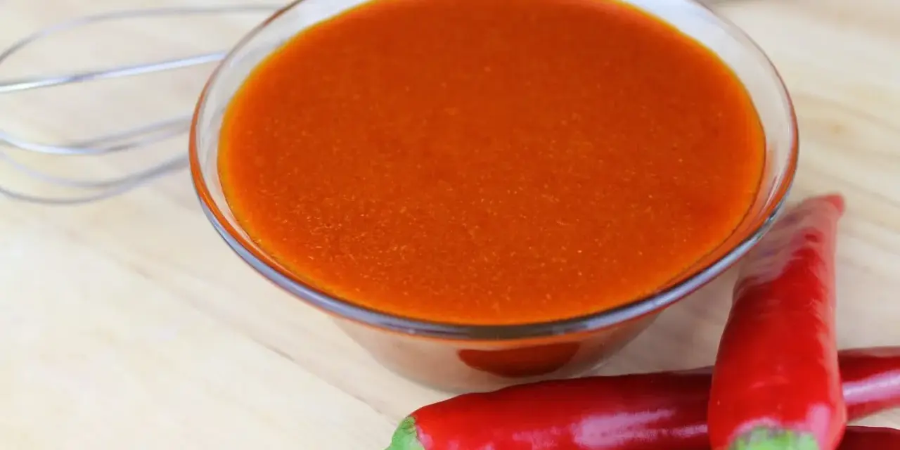 Schüssel mit leuchtend orangeroter Buffalo Sauce, daneben rote Chilis und ein Schneebesen. Perfekt für Flügel!