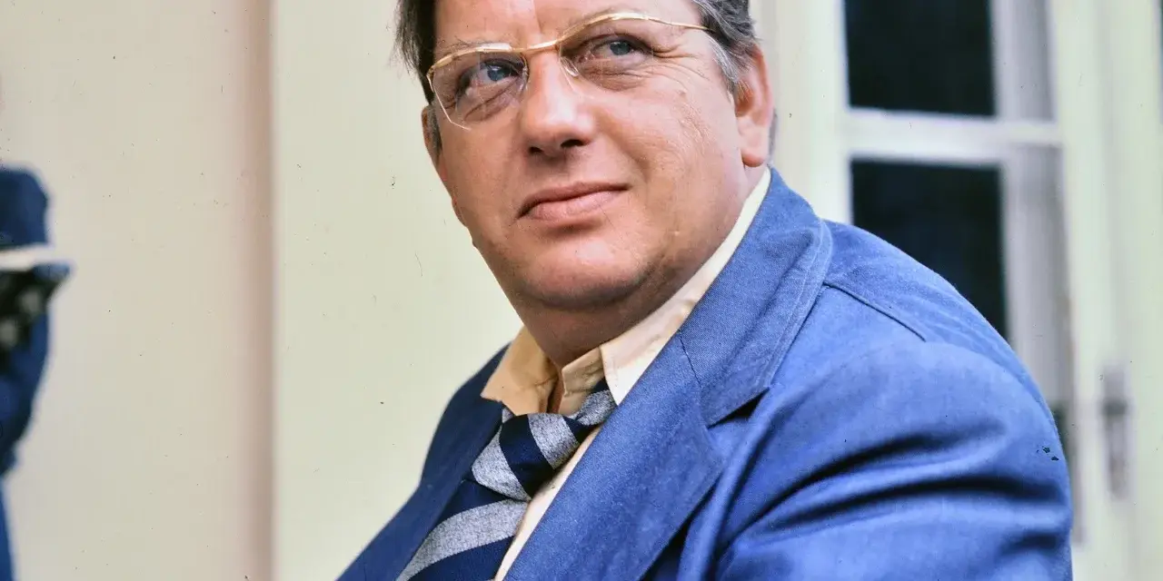 Portret Mariusza Dmochowskiego w okularach i niebieskiej marynarce. W tle okno.