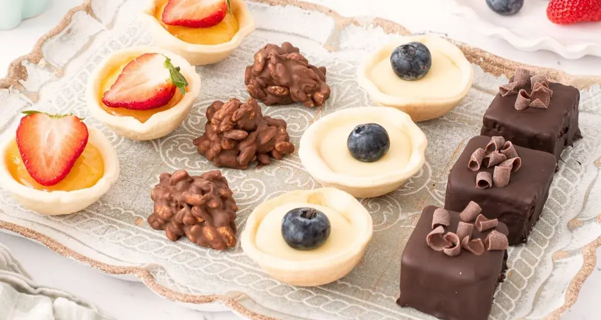Bandeja con variedad de petit fours: tartaletas de fresa y arándano, bombones de chocolate y dulces de frutos secos.