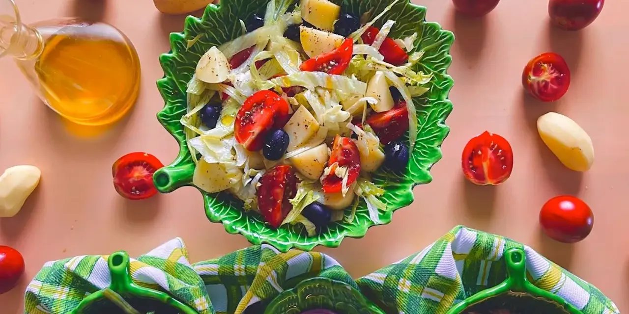 Un'insalata di patate napoletana colorata con pomodorini, olive e lattuga, servita in una ciotola a forma di foglia.
