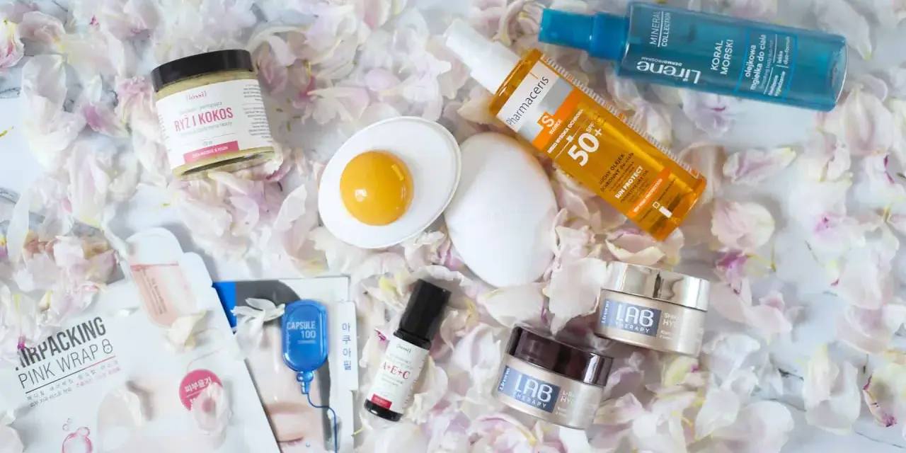 Kosmetyki do pielęgnacji: kremy, serum, mgiełka do ciała, olejek ochronny i peeling ryżowy. Całość ułożona na płatkach kwiatów, tworząc wiosenny, roc.