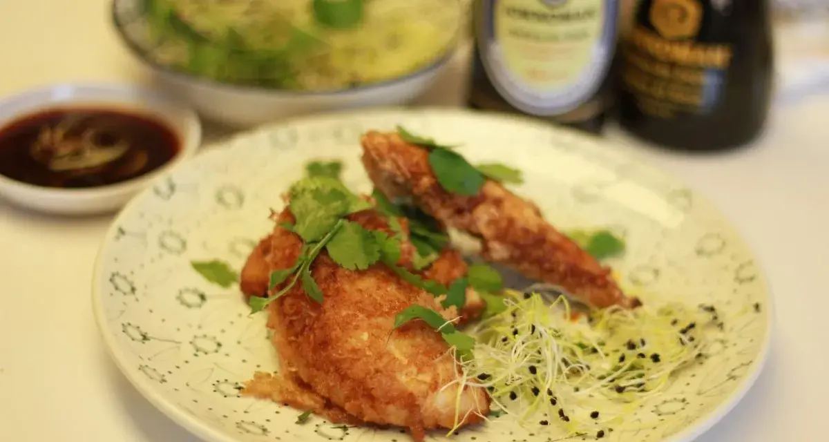 Crujiente solomillo de pollo empanado, adornado con cilantro fresco y brotes, servido con salsa y un cuenco de ensalada.