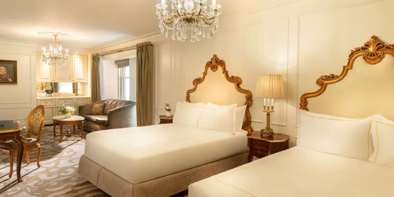 Luksusowy pokój z dwoma łóżkami w hotelu Plaza w Nowym Jorku, z kryształowym żyrandolem i złotymi zdobieniami. Zastanawiasz się, ile kosztuje noc w hotelu Plaza w Nowym Jorku?