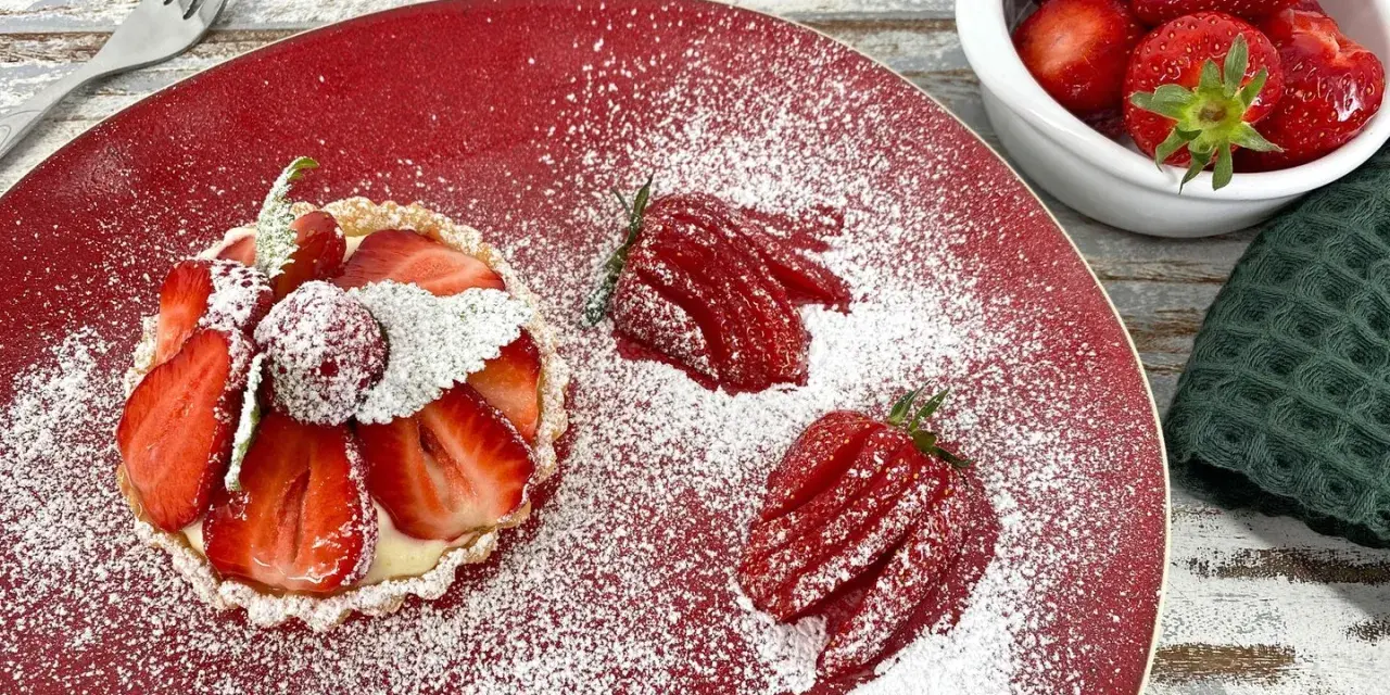 Zuckersüße Erdbeer Tartelettes, bestäubt mit Puderzucker, auf rotem Teller. Daneben frische Erdbeeren und eine Gabel.