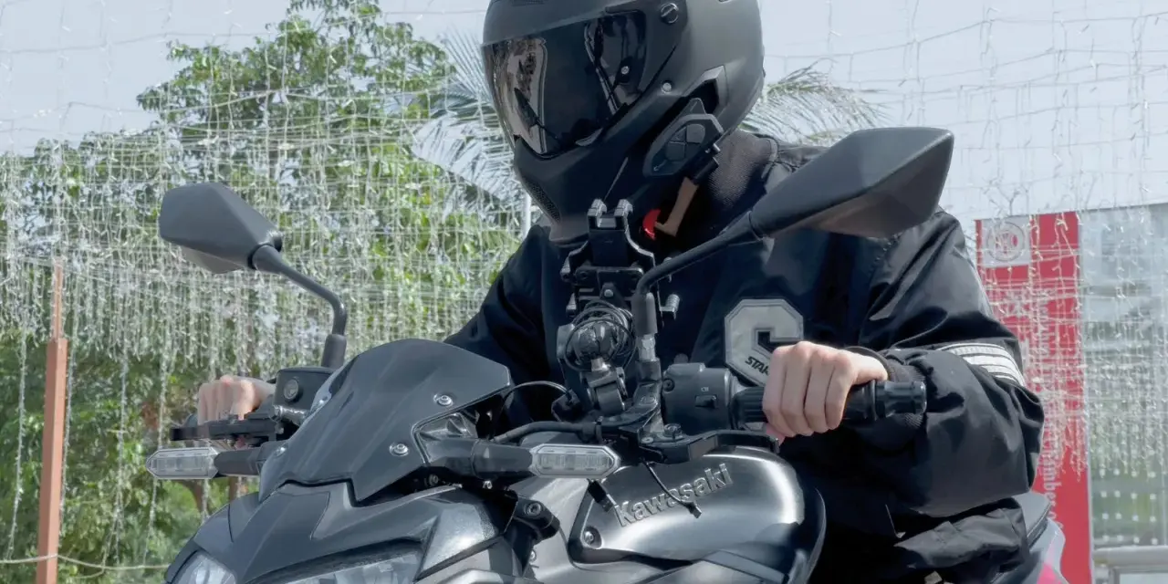 Motocyklista w kasku siedzi na motocyklu Kawasaki, z zamontowanym interkomem na kasku.