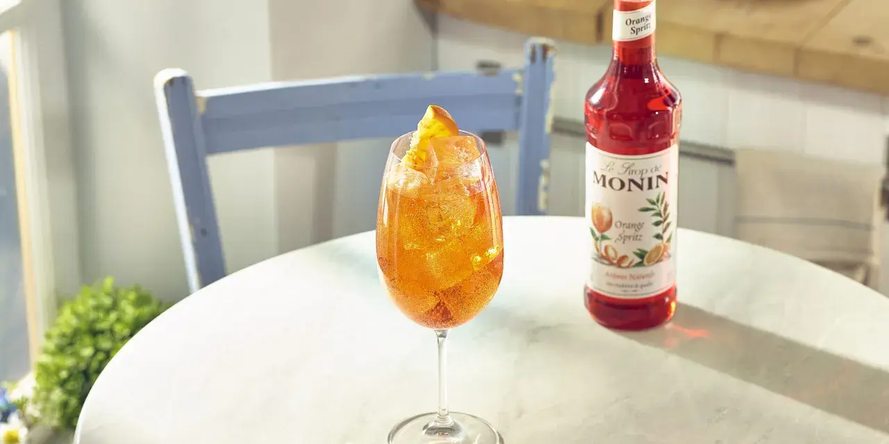 Orzeźwiający drink z syropem Monin Orange Spritz, lodem i pomarańczą. Idealny przepis na letnie popołudnie.