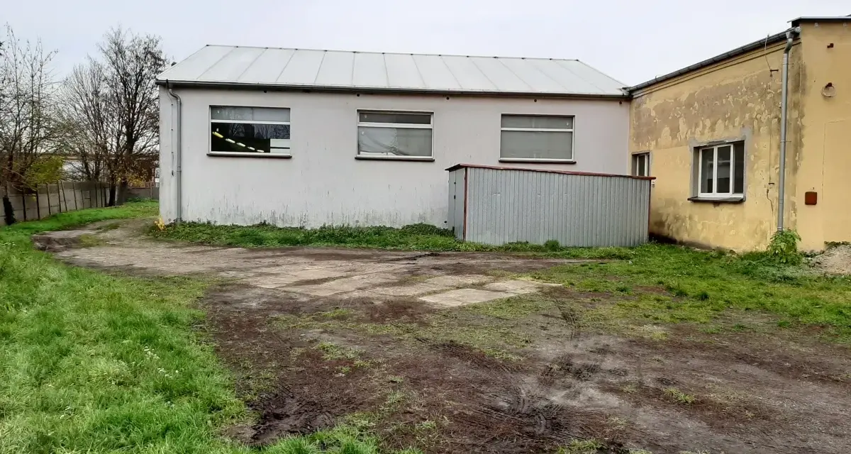 Teren wokół budynków jest nierówny, z błotnistymi śladami i trawą. Widać tu różne formy terenu, od płaskich placów po lekko nachylone trawniki.