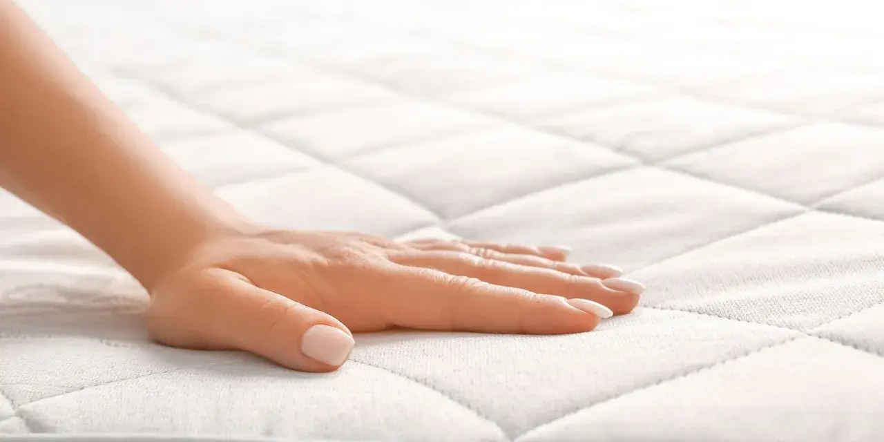 Main d'une femme effleurant un matelas orthopédique, offrant un confort et un soutien idéaux pour un sommeil réparateur.