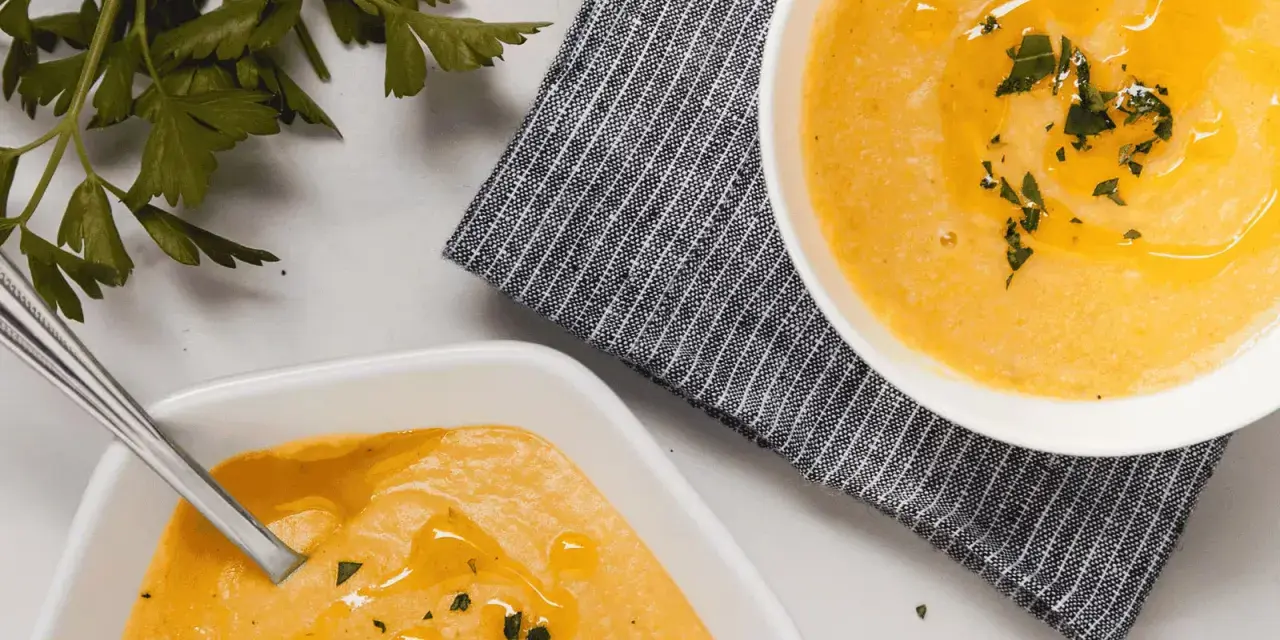 Deux bols de velouté de butternut facile, ornés d'huile d'olive et de persil frais, prêts à être dégustés.