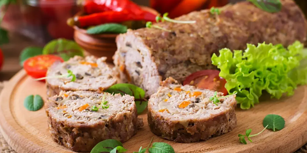 Pokrojone zrazy z mięsa mielonego z warzywami na desce, obok sałata, pomidory i papryczki chili.