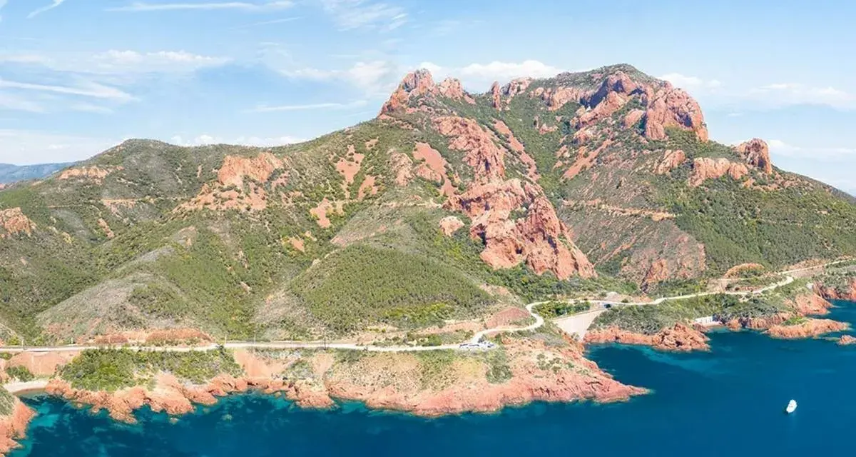 Strada panoramica sulla Corniche de l'Esterel, con montagne rosse e mare blu intenso.