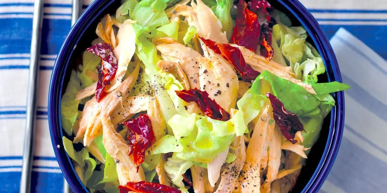 Insalata di pollo lesso con lattuga croccante e pomodori secchi, condita con pepe nero macinato.